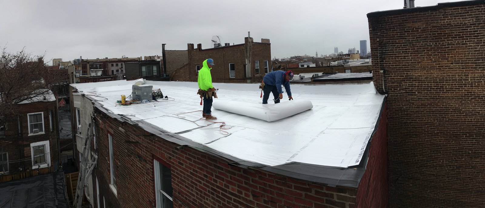Hearth Roofing crew rolling out a new white TPO membrane over tapered insulation on a Queens commercial flat roof