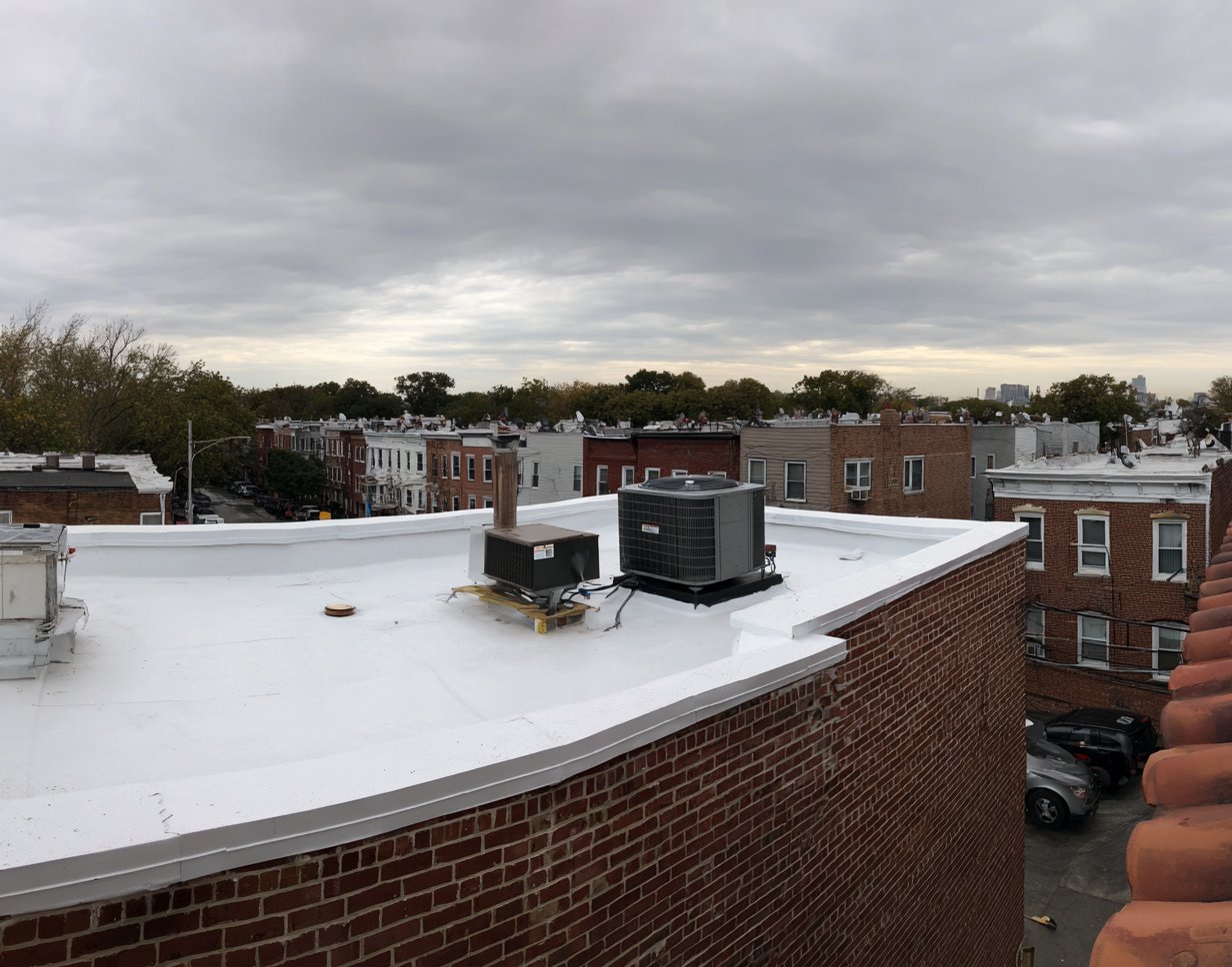 Wide commercial flat roof in Queens with a white membrane, parapet walls, rooftop HVAC units and a roof drain