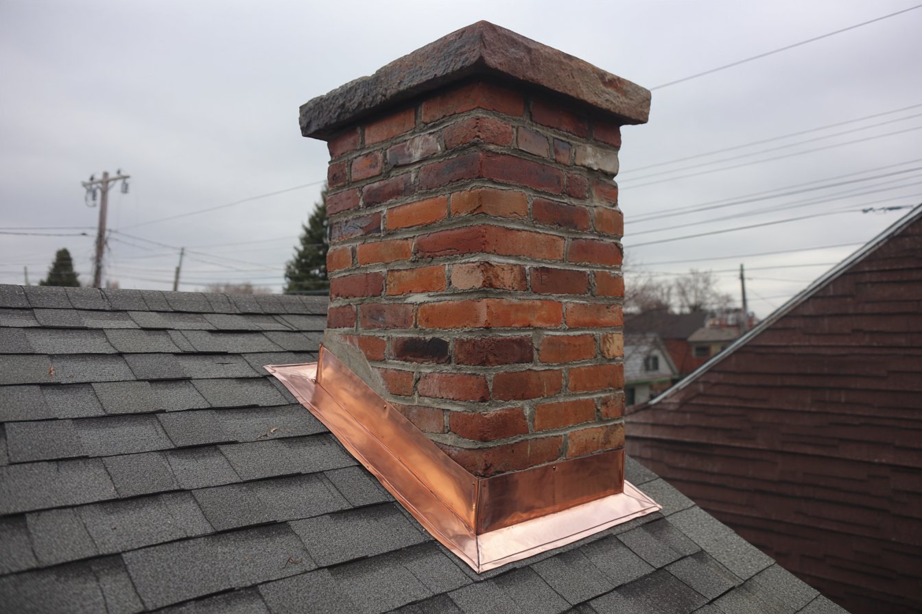 After: new step flashing and copper counter flashing set into the mortar joints of a brick chimney on an Astoria row house