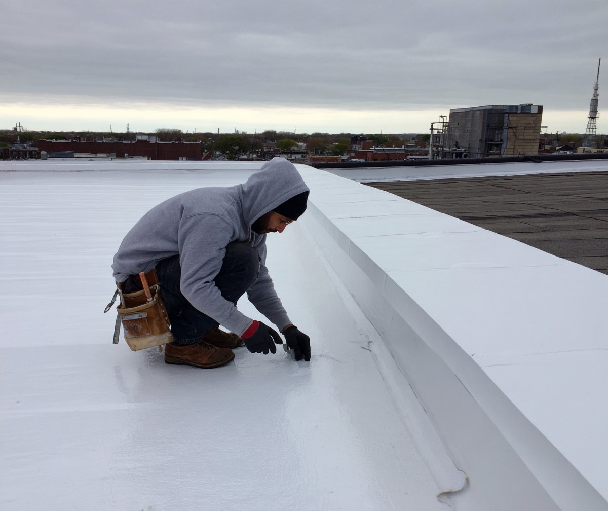Roofer tracing a leak across the membrane of a flat commercial roof in Queens